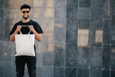 Kentsel şehir arka plan karşı beyaz tekstil eko çanta tutan genç adam. . Ekoloji veya çevre koruma kavramı. Sahte için beyaz eko çanta.