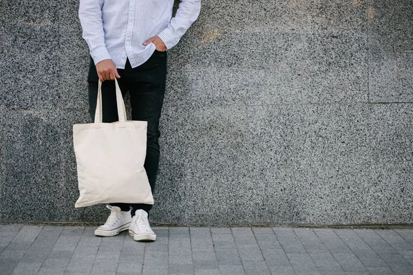 Ung man innehar vit textil Eco Bag mot Urban City bakgrund. . Ekologin eller miljöskydds konceptet. Vit Eco Bag för mock-up. — Stockfoto