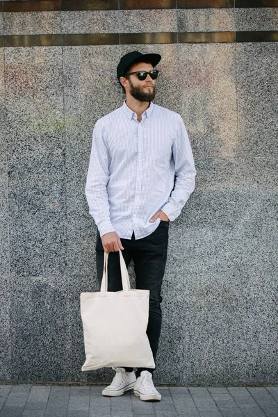 Jonge man Holding witte textiel Eco tas tegen stedelijke stad achtergrond. . Ecologie of milieubescherming concept. Witte Eco-tas voor mock up. — Stockfoto