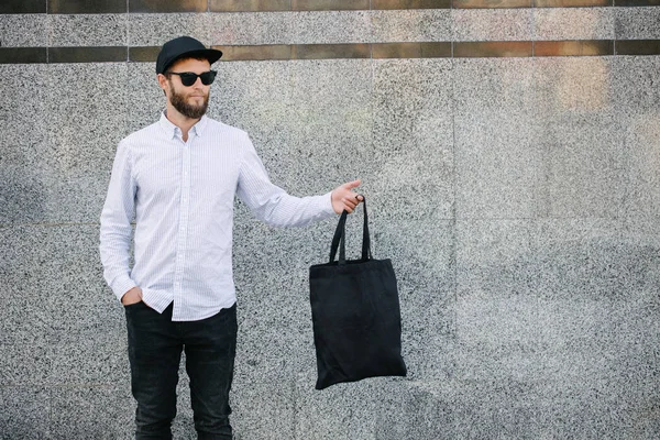 Kentsel şehir arka plan karşı siyah tekstil eko çanta tutan genç adam. . Ekoloji veya çevre koruma kavramı. Tasarım veya logo sahte için siyah eko çanta