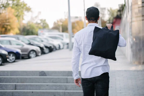 Νέος άνθρωπος που κατέχει μαύρη υφαντουργική τσάντα Eco κατά του αστικού ιστορικού της πόλης. . Οικολογία ή έννοια προστασίας του περιβάλλοντος. Μαύρη τσάντα Eco για το σχεδιασμό ή το λογότυπο σας — Φωτογραφία Αρχείου