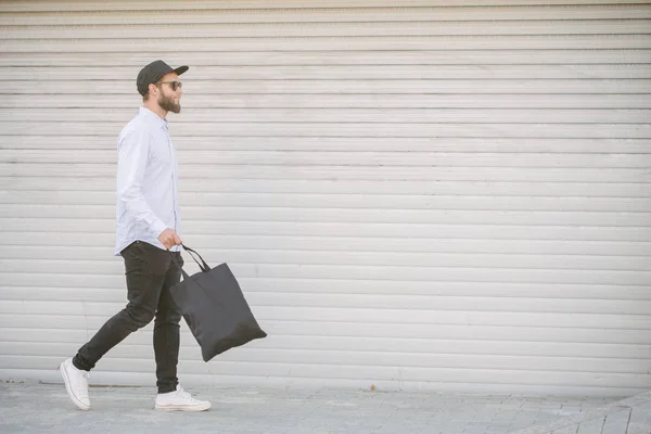 Joven sosteniendo bolso ecológico textil negro contra fondo urbano de la ciudad. .. Ecología o concepto de protección del medio ambiente. Bolso ecológico negro para su diseño o logotipo maqueta — Foto de Stock