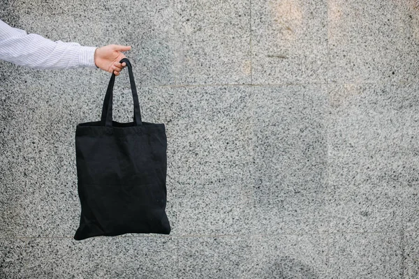 Fiatal férfi gazdaság fekete textil Eco táska ellen városi város háttérben. . Ökológiai vagy környezetvédelmi koncepció. Fekete öko táska a design vagy logó gúnyolódni — Stock Fotó