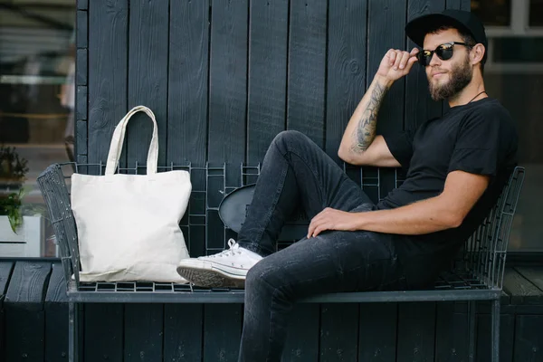 Joven sosteniendo bolso ecológico textil blanco contra fondo urbano. .. Ecología o concepto de protección del medio ambiente. Bolso ecológico blanco para maqueta . — Foto de Stock