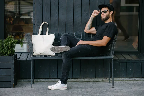 Kentsel şehir arka plan karşı beyaz tekstil eko çanta tutan genç adam. . Ekoloji veya çevre koruma kavramı. Sahte için beyaz eko çanta.