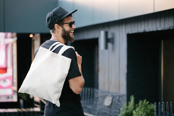 Fiatal férfi gazdaság fehér textil Eco táska ellen városi város háttérben. . Ökológiai vagy környezetvédelmi koncepció. Fehér öko táska a modell fel. — Stock Fotó