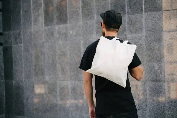Kentsel şehir arka plan karşı beyaz tekstil eko çanta tutan genç adam. . Ekoloji veya çevre koruma kavramı. Sahte için beyaz eko çanta.