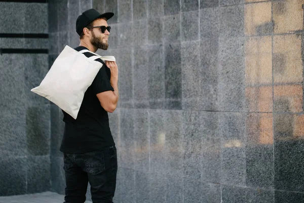 Kentsel şehir arka plan karşı beyaz tekstil eko çanta tutan genç adam. . Ekoloji veya çevre koruma kavramı. Sahte için beyaz eko çanta.