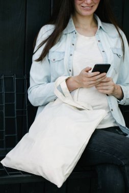 Kentsel şehir arka plan karşı beyaz tekstil eko çanta tutan kadın. . Ekoloji veya çevre koruma kavramı. Sahte için beyaz eko çanta.