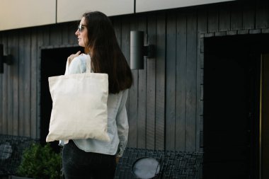 Kentsel şehir arka plan karşı beyaz tekstil eko çanta tutan kadın. . Ekoloji veya çevre koruma kavramı. Sahte için beyaz eko çanta.