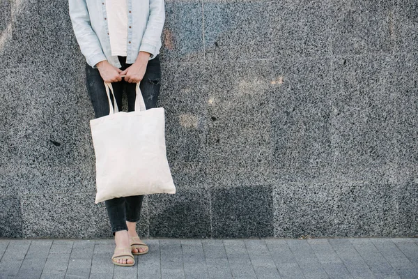 Mujer sosteniendo bolso ecológico textil blanco contra fondo urbano de la ciudad. .. Ecología o concepto de protección del medio ambiente. Bolso ecológico blanco para maqueta . —  Fotos de Stock
