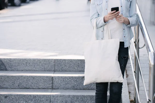 Frau mit weißer Textil-Öko-Tasche vor städtischem Hintergrund. . Ökologie oder Umweltschutzkonzept. weiße Öko-Tasche für Attrappen. — Stockfoto
