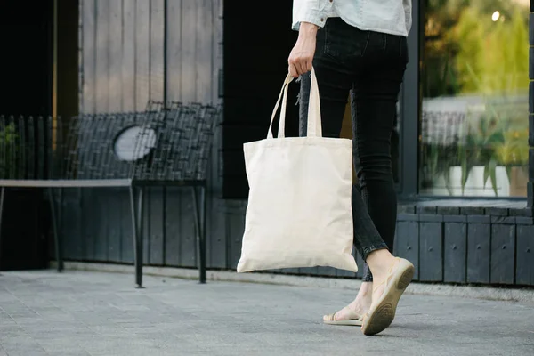 Mujer sosteniendo bolso ecológico textil blanco contra fondo urbano de la ciudad. .. Ecología o concepto de protección del medio ambiente. Bolso ecológico blanco para maqueta . —  Fotos de Stock