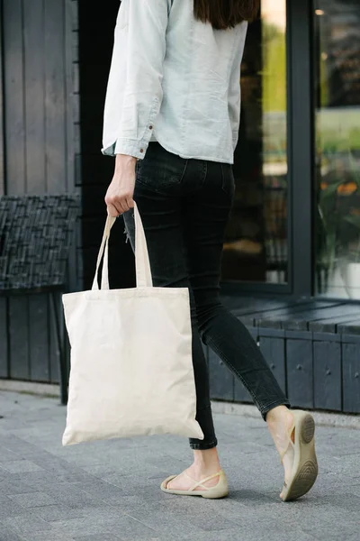 Donna in possesso di tessuto bianco eco bag sullo sfondo urbano della città. . Ecologia o concetto di protezione dell'ambiente. Sacchetto eco bianco per mock up . — Foto Stock