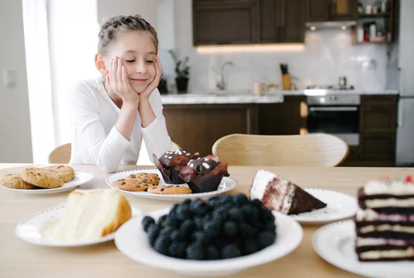 KIG meisje glimlachend tijdens het kijken naar taarten thuis — Stockfoto