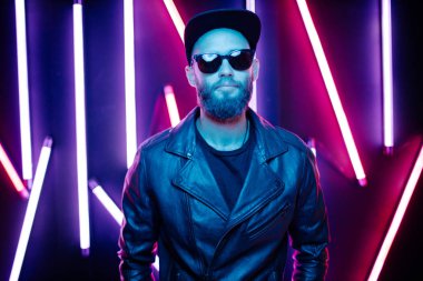 Şehir sokaklarında hipster yakışıklı adam Neon işaretler tarafından aydınlatılmış olmak. O siyah kap, kot pantolon ve güneş gözlüğü ile deri motosikletçi ceket veya asimetrik fermuar ceket giyiyor.