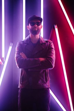 Şehir sokaklarında hipster yakışıklı adam Neon işaretler tarafından aydınlatılmış olmak. O siyah kap, kot pantolon ve güneş gözlüğü ile deri motosikletçi ceket veya asimetrik fermuar ceket giyiyor.