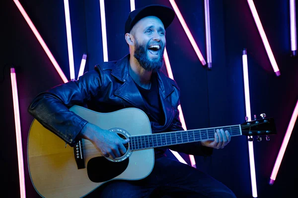 Τραγουδιστής και κιθαρίστας τραγουδώντας σε μια σκηνή με φώτα νέον. Είναι ροκάς και φοράει δερμάτινο μπουφάν ή ασύμμετρο φερμουάρ με μαύρο καπάκι, Τζιν. — Φωτογραφία Αρχείου