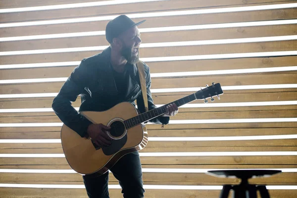 Cantor e guitarrista cantando em um palco com luzes de néon. Ele é um roqueiro e ele está vestindo jaqueta de couro motociclista ou jaqueta zip assimétrica com boné preto, jeans . — Fotografia de Stock