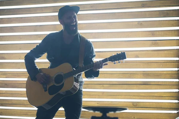 Sänger und Gitarrist singen auf einer Bühne mit Neonlichtern. er ist Rocker und trägt eine Motorradjacke aus Leder oder eine asymmetrische Reißverschlussjacke mit schwarzer Kappe, Jeans. — Stockfoto