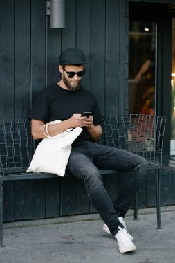 Kentsel şehir arka plan karşı beyaz tekstil eko çanta tutan genç adam. Ekoloji veya çevre koruma kavramı. Sahte için beyaz eko çanta.