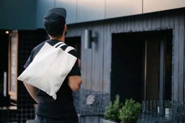 Kentsel şehir arka plan karşı beyaz tekstil eko çanta tutan genç adam. Ekoloji veya çevre koruma kavramı. Sahte için beyaz eko çanta.