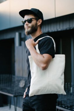 Kentsel şehir arka plan karşı beyaz tekstil eko çanta tutan genç adam. Ekoloji veya çevre koruma kavramı. Sahte için beyaz eko çanta.