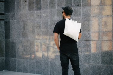 Kentsel şehir arka plan karşı beyaz tekstil eko çanta tutan genç adam. Ekoloji veya çevre koruma kavramı. Sahte için beyaz eko çanta.