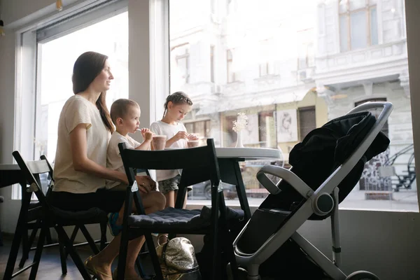 Madre con bambini che beve cioccolata calda e latte macchiato in una caffetteria locale. Sorridono e si divertono. Concetto di maternità — Foto Stock