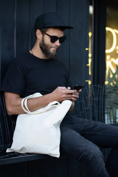 Junger Mann mit weißer Textil-Öko-Tasche vor städtischem Hintergrund. Ökologie oder Umweltschutzkonzept. weiße Öko-Tasche für Attrappen. — Stockfoto