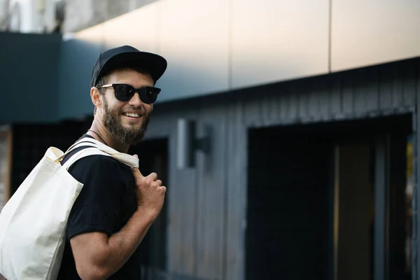 Ung man innehar vit textil Eco Bag mot Urban City bakgrund. Ekologin eller miljöskydds konceptet. Vit Eco Bag för mock-up. — Stockfoto