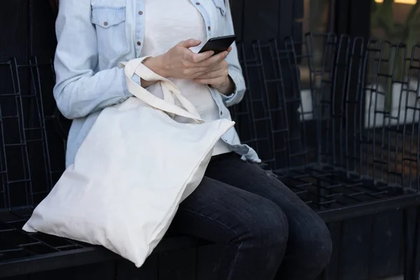 Vrouw Holding witte textiel Eco-tas tegen stedelijke stad achtergrond. Ecologie of milieubescherming concept. Witte Eco-tas voor mock up. — Stockfoto