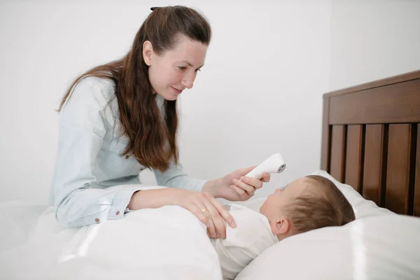 A mulher mede a temperatura. O miúdo está doente deitado na cama. — Fotografia de Stock