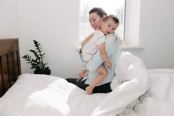Matka a dítě se baví v ložnici/skáčou a objímají — Stock fotografie