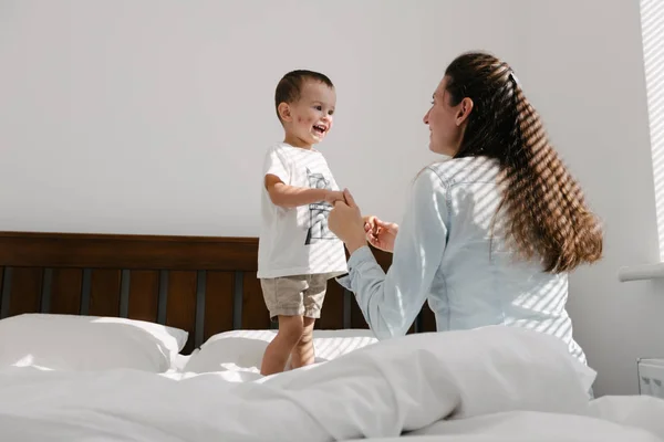 Madre e hijo divirtiéndose en el dormitorio / Están saltando y abrazándose —  Fotos de Stock