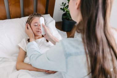 Anne, bir çocuk kızın sıcaklığını kontrol ediyor. Çocuk yatakta yatarken hasta.