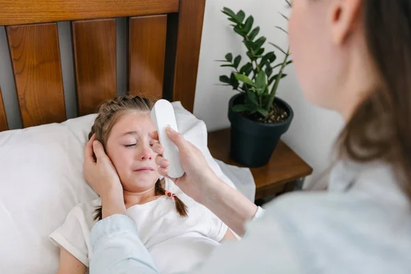 Mor kontrollera temperaturen hos en barnflicka. Ungen är sjukt liggande i sängen — Stockfoto