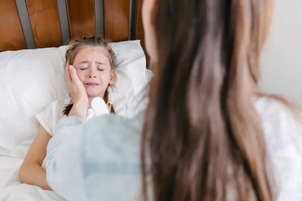 Kid gråter i sängen. Mamma försöker lugna henne. Ömhet cincept — Stockfoto