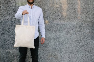 Kentsel şehir arka plan karşı beyaz tekstil eko çanta tutan genç adam. Ekoloji veya çevre koruma kavramı. Sahte için beyaz eko çanta.