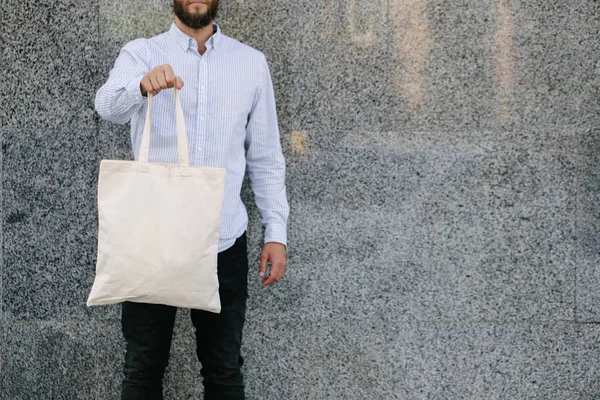 Junger Mann mit weißer Textil-Öko-Tasche vor städtischem Hintergrund. Ökologie oder Umweltschutzkonzept. weiße Öko-Tasche für Attrappen. — Stockfoto