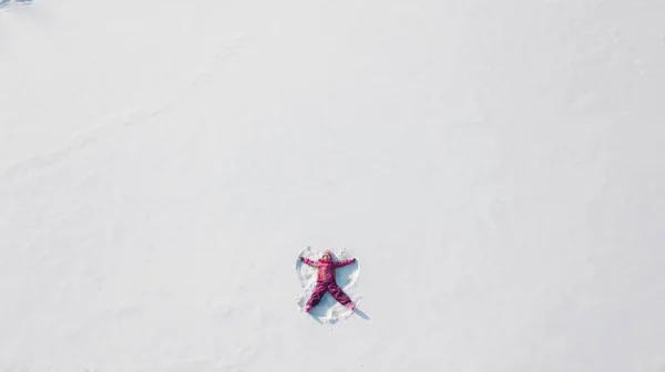 Kind auf einem Schnee, der einen Schneengel macht. Luftaufnahme von oben. sie trägt rote Kleidung — Stockfoto