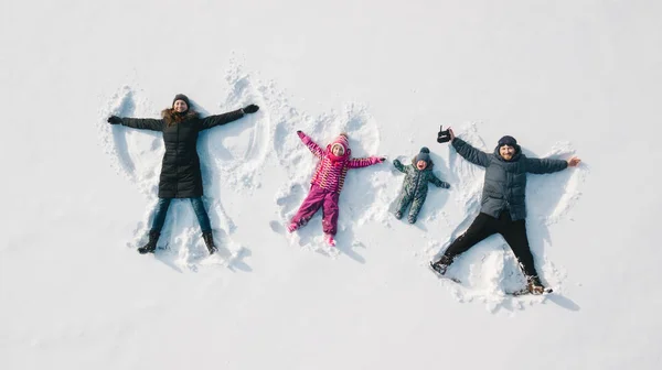 Família a fazer um anjo da neve. Vista aérea. Mãe e pai e criança fazendo um anjo da neve — Fotografia de Stock