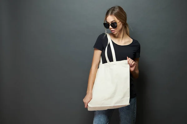 Jonge vrouw Holding witte textiel Eco-tas tegen grijze achtergrond. Ecologie of milieubescherming concept. Witte Eco-tas voor mock up. — Stockfoto