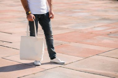 Kentsel şehir arka plan karşı beyaz tekstil eko çanta tutan genç adam. Ekoloji veya çevre koruma kavramı. Sahte için beyaz eko çanta.