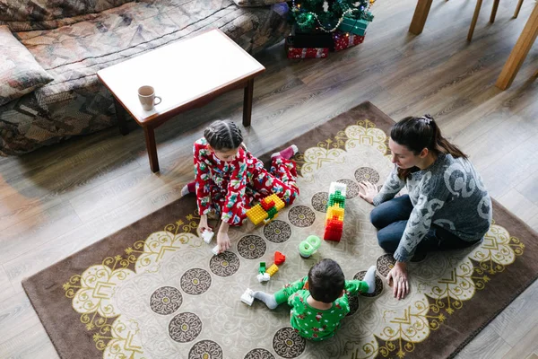 Kinderen met moeder spelen binnen naast een kerstboom in een pyjama — Stockfoto