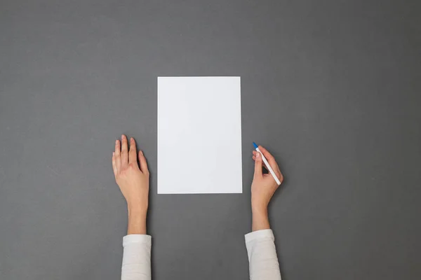 White sheet of paper for your text. Woman holding an empty sheet of paper over gray texture. Overhead view