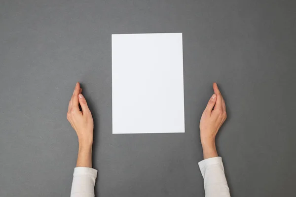 Biała kartka do twojego SMS-a. Kobieta trzymająca pustą kartkę papieru na szarej fakturze. Widok nad głową — Zdjęcie stockowe
