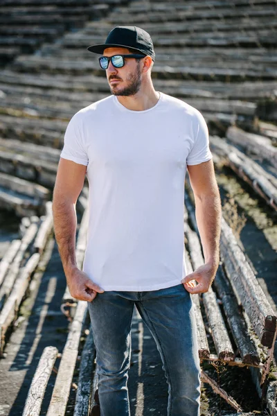 Modelo masculino bonito Hipster com barba vestindo t-shirt branca em branco e um boné de beisebol com espaço para o seu logotipo ou design em estilo urbano casual — Fotografia de Stock