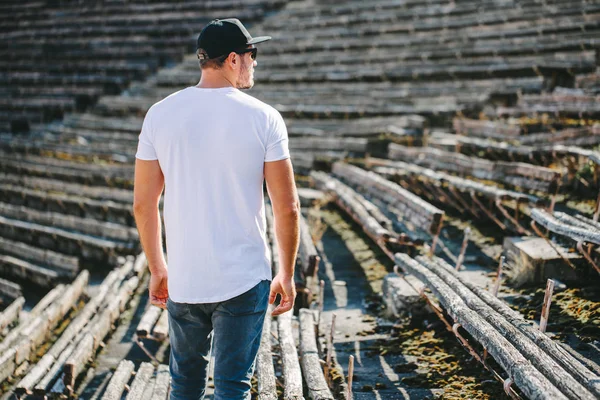 Hipster pohledný mužský model s vousy v bílém prázdném tričku a baseballovou čepicí s prostorem pro vaše logo nebo design v neformálním městském stylu — Stock fotografie