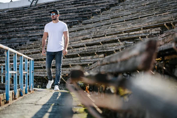 Hipster handsome male model with beard wearing white blank t-shirt and a baseball cap with space for your logo or design in casual urban style — Stock Photo, Image